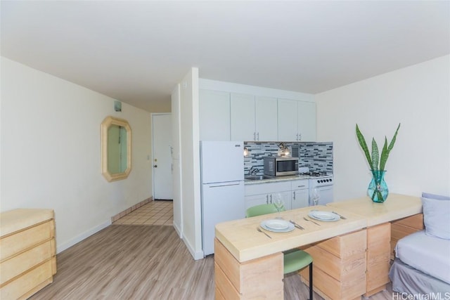 kitchen featuring light hardwood / wood-style floors, white cabinetry, white appliances, and a breakfast bar area