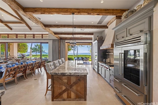 kitchen with a kitchen bar, beam ceiling, a center island with sink, and gray cabinetry