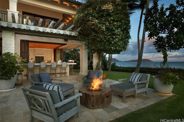 patio terrace at dusk featuring a fire pit, a balcony, a bar, and a water and mountain view