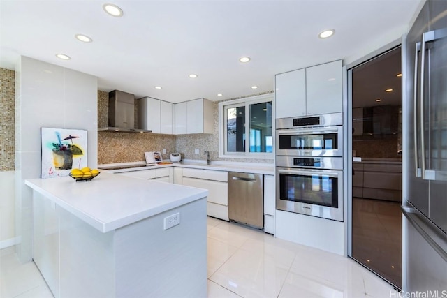 kitchen featuring wall chimney range hood, sink, tasteful backsplash, white cabinetry, and stainless steel appliances