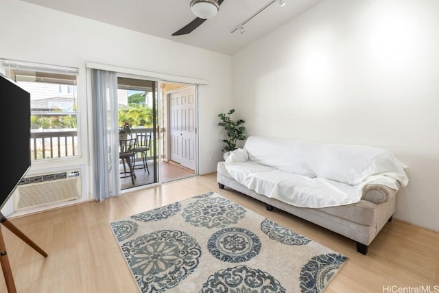 living room featuring a wall mounted AC, wood-type flooring, track lighting, and ceiling fan