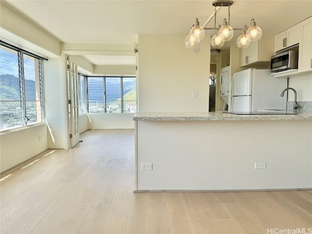 kitchen with freestanding refrigerator, stainless steel microwave, a sink, and light wood-style flooring