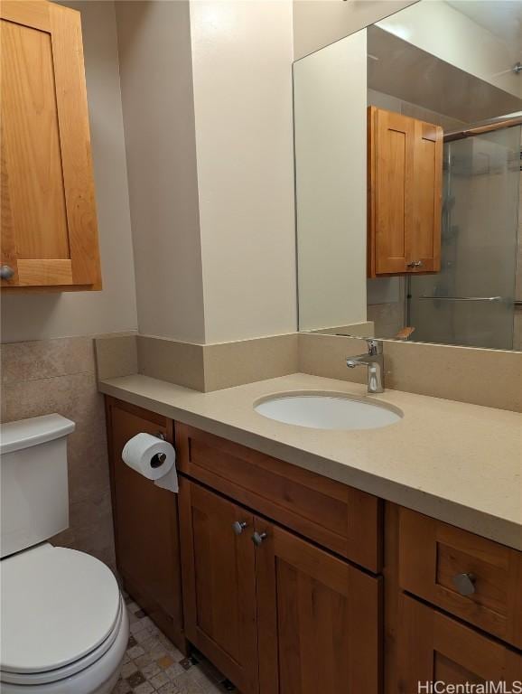 bathroom with vanity, a shower with door, toilet, and tile walls