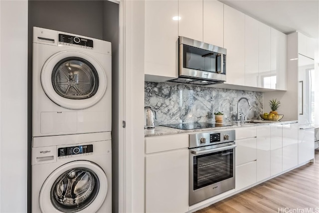 kitchen featuring stacked washer and dryer, light hardwood / wood-style flooring, light stone countertops, white cabinetry, and stainless steel appliances