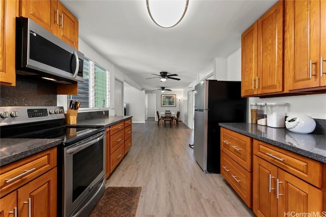 kitchen featuring ceiling fan, dark stone countertops, light wood-type flooring, and appliances with stainless steel finishes