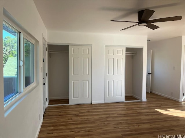 unfurnished bedroom featuring multiple closets, dark hardwood / wood-style floors, and ceiling fan