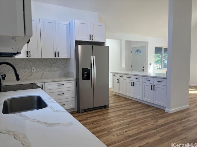 kitchen featuring sink, white cabinets, stainless steel fridge, decorative backsplash, and light stone countertops