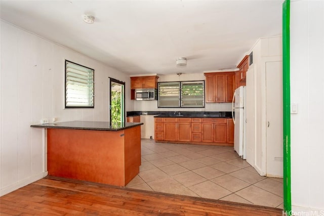 kitchen featuring dark stone counters, kitchen peninsula, light hardwood / wood-style floors, and white refrigerator