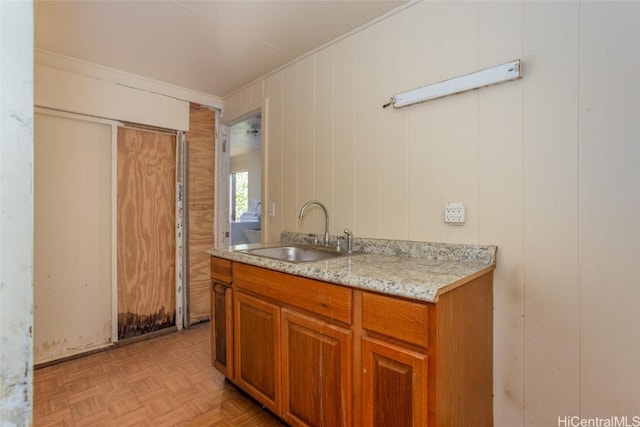 kitchen with wood walls, sink, ornamental molding, light stone countertops, and light parquet flooring