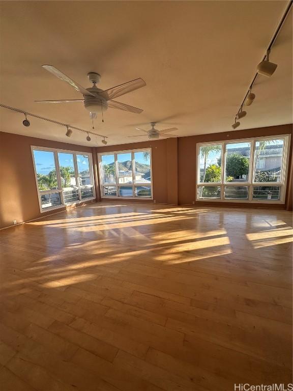 spare room featuring ceiling fan, a wealth of natural light, rail lighting, and hardwood / wood-style flooring