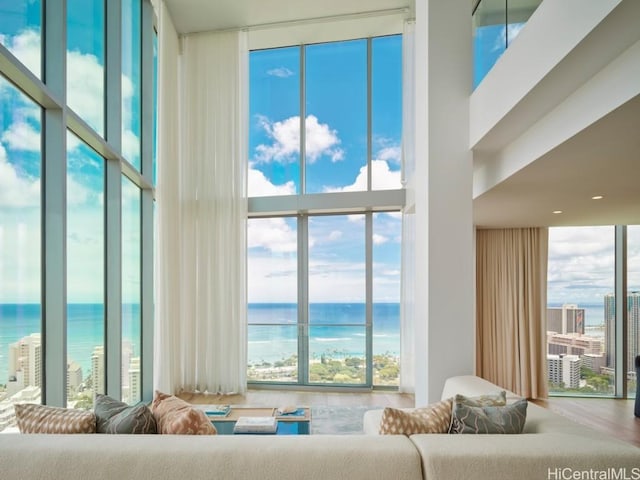 living room with expansive windows, a towering ceiling, a water view, and hardwood / wood-style flooring