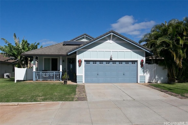 view of front of home with covered porch, a garage, a front yard, and solar panels