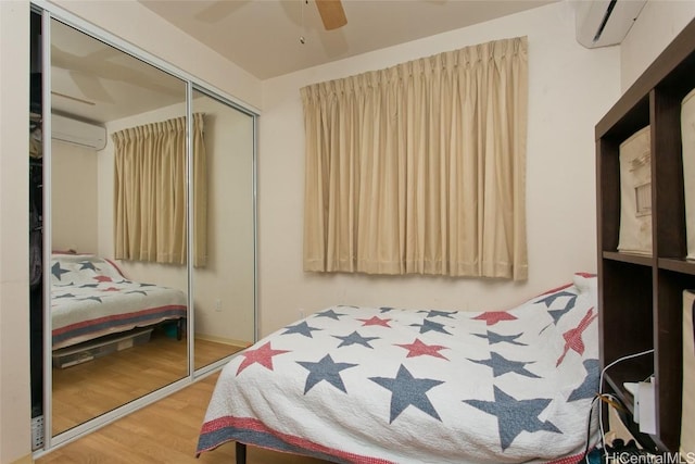 bedroom featuring ceiling fan, wood-type flooring, an AC wall unit, and a closet