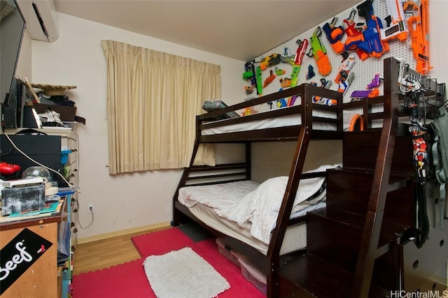 bedroom with a wall mounted air conditioner and wood-type flooring