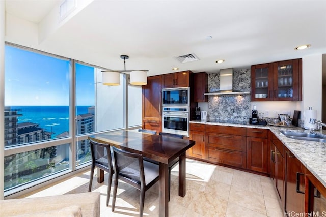 kitchen with appliances with stainless steel finishes, sink, wall chimney range hood, a water view, and hanging light fixtures