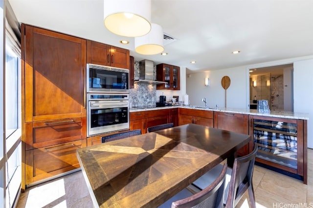 kitchen featuring built in microwave, wall chimney range hood, wine cooler, light stone counters, and oven