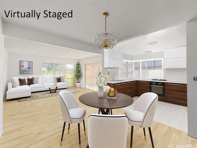 dining space with a chandelier, sink, light hardwood / wood-style floors, and a textured ceiling