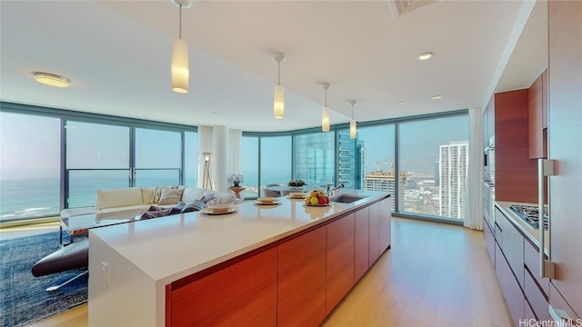 kitchen featuring decorative light fixtures, expansive windows, light wood-type flooring, and sink