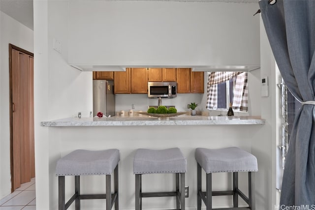 kitchen with kitchen peninsula, a breakfast bar area, light tile patterned floors, and appliances with stainless steel finishes