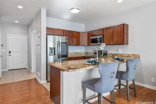 kitchen featuring light hardwood / wood-style flooring, a breakfast bar, stainless steel appliances, light stone counters, and kitchen peninsula