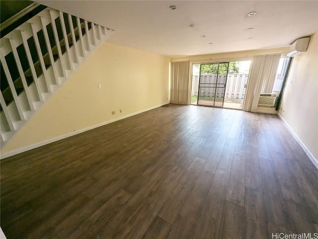 unfurnished living room featuring an AC wall unit, baseboards, and dark wood-style flooring