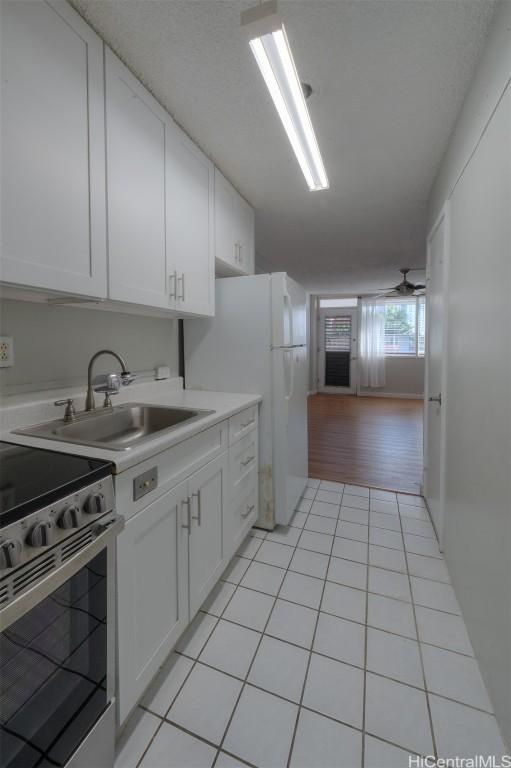 kitchen featuring stainless steel range, sink, light tile patterned flooring, white refrigerator, and white cabinets