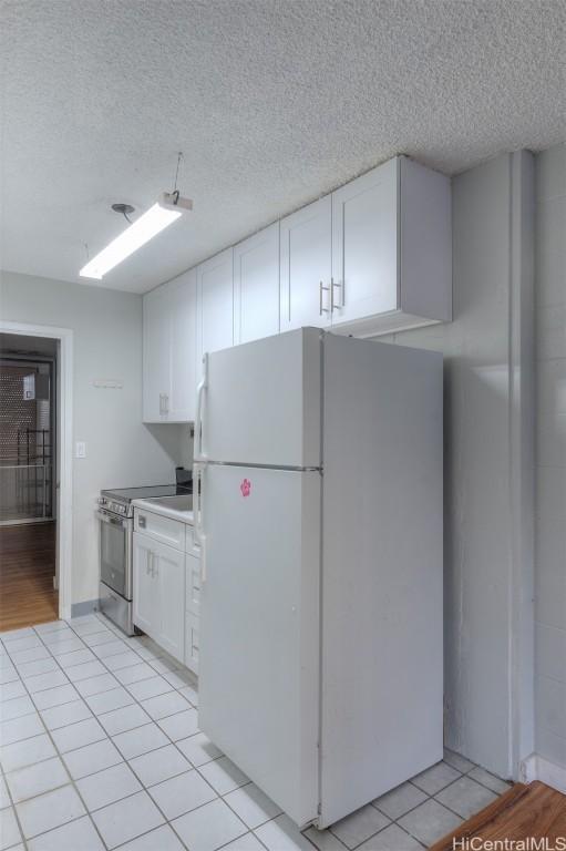 kitchen with electric stove, white cabinetry, white fridge, and light tile patterned floors