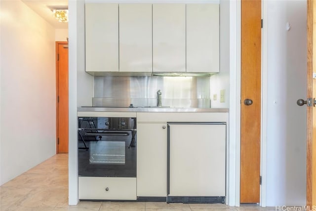 kitchen with black oven, stainless steel counters, sink, and white cabinets