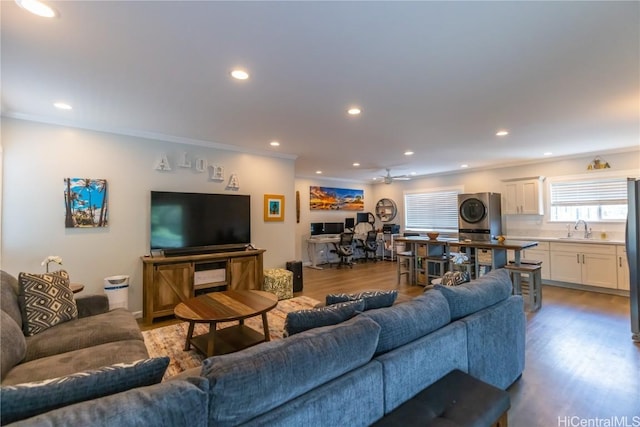 living room with sink, ornamental molding, light hardwood / wood-style floors, and stacked washer and dryer