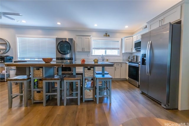 kitchen featuring crown molding, appliances with stainless steel finishes, white cabinetry, stacked washer / drying machine, and light wood-type flooring