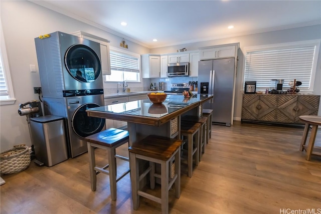 kitchen featuring sink, light hardwood / wood-style flooring, stainless steel appliances, stacked washer and clothes dryer, and ornamental molding