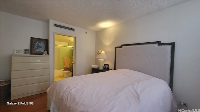 bedroom featuring ensuite bath, wood-type flooring, and a textured ceiling