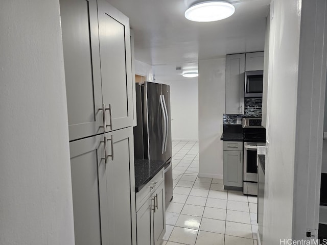 kitchen featuring decorative backsplash, appliances with stainless steel finishes, gray cabinetry, light tile patterned floors, and dark stone countertops