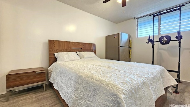 bedroom featuring stainless steel fridge, hardwood / wood-style flooring, and ceiling fan