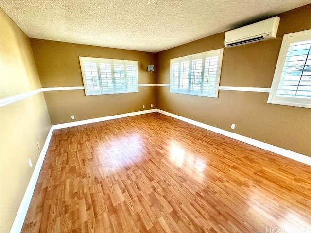 unfurnished room with a wall unit AC, a textured ceiling, and hardwood / wood-style flooring