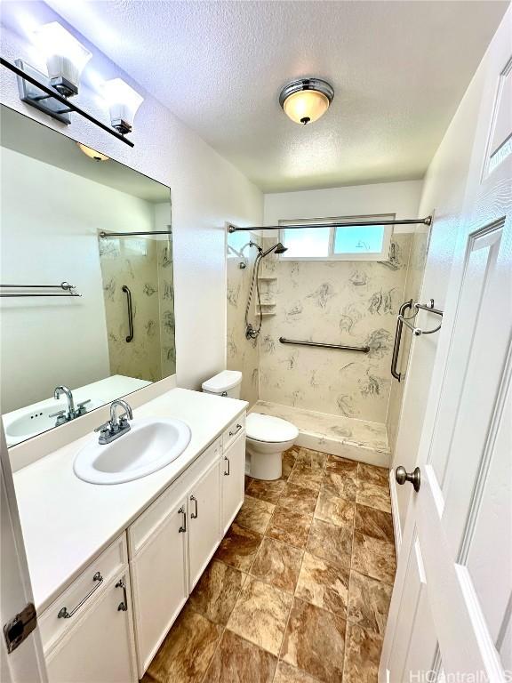 bathroom with vanity, toilet, a tile shower, and a textured ceiling