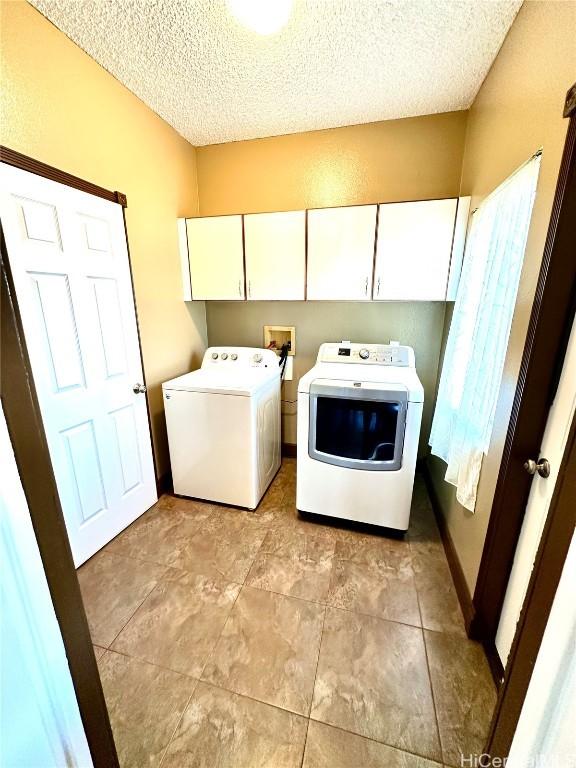 washroom featuring cabinets, a textured ceiling, light tile patterned flooring, and washing machine and clothes dryer