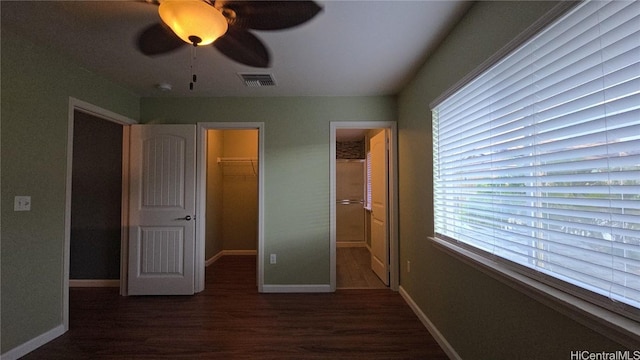 unfurnished bedroom with a walk in closet, ceiling fan, a closet, and dark wood-type flooring