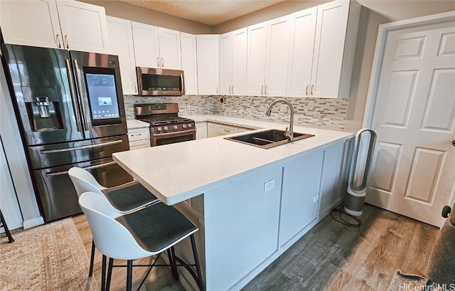 kitchen with kitchen peninsula, appliances with stainless steel finishes, a kitchen breakfast bar, sink, and white cabinetry