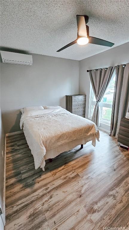 bedroom with wood-type flooring, a textured ceiling, a wall unit AC, and ceiling fan