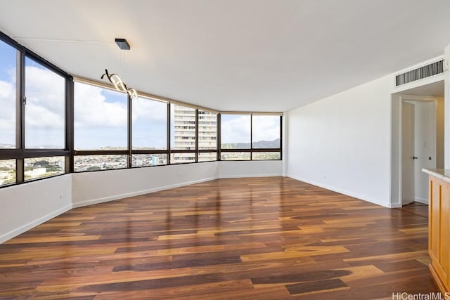 spare room featuring a city view, dark wood finished floors, visible vents, and baseboards