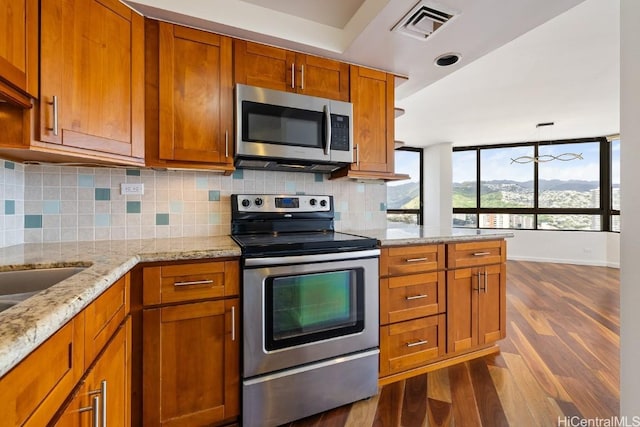 kitchen featuring visible vents, light stone counters, brown cabinets, dark wood-style flooring, and stainless steel appliances