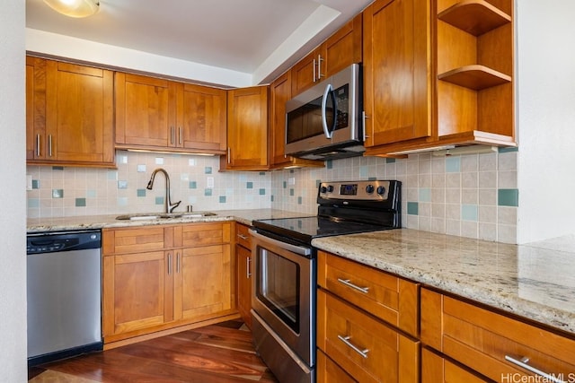 kitchen with light stone counters, dark wood-style floors, appliances with stainless steel finishes, brown cabinetry, and a sink