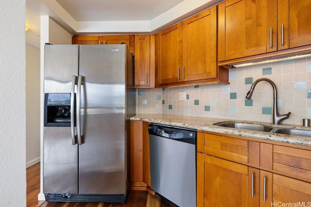 kitchen featuring appliances with stainless steel finishes, brown cabinetry, a sink, and light stone countertops