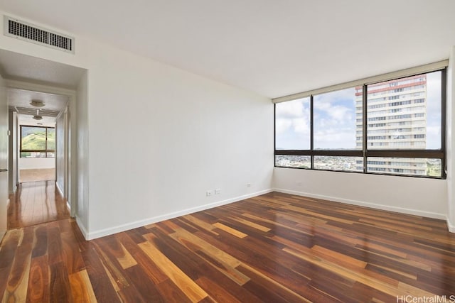 spare room with a city view, dark wood-type flooring, visible vents, and baseboards