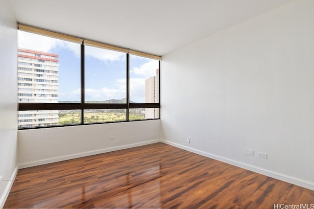 unfurnished room with a city view, dark wood-style flooring, and baseboards