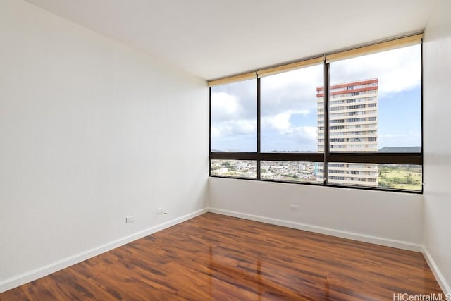 spare room with dark wood-type flooring, a city view, and baseboards