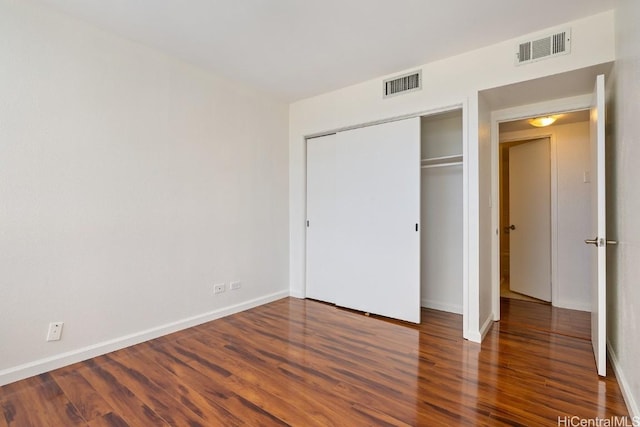 unfurnished bedroom with a closet, dark wood-style flooring, visible vents, and baseboards