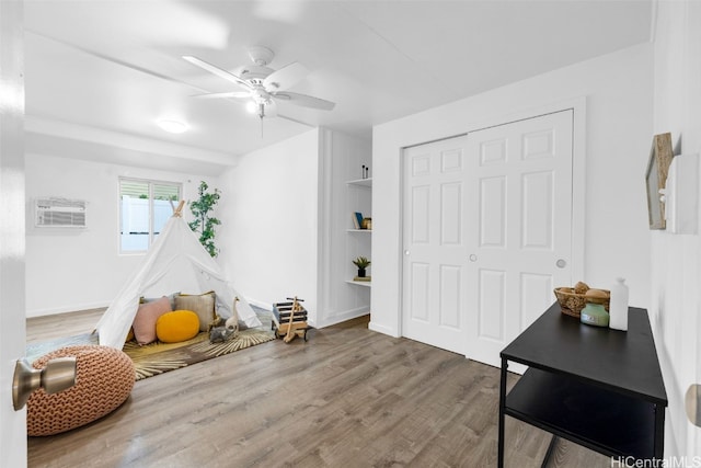 playroom featuring hardwood / wood-style flooring, a wall unit AC, and ceiling fan