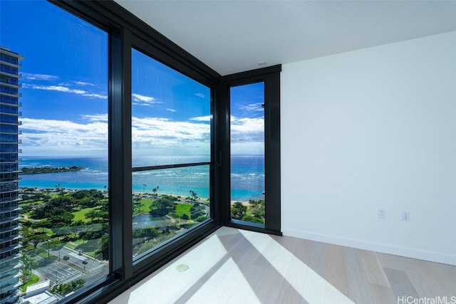 spare room with floor to ceiling windows, a water view, and light hardwood / wood-style flooring